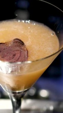 Barmen yavaş çekimde kokteyl bardağına martini döküyor. Alkol yavaş yavaş cam yeşil zeytin döker.
