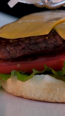 Şef arka planda servis tabağında lezzetli bir burger yapıyor. Köfteli çizburger, peynir, domates, soğan, kızarmış ekmek, marul, sos..