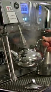 Kafeteryadaki profesyonel espresso makinesini ayarlayan, buhar çubuğu kullanan, arka plandaki tanınamayan iş arkadaşını yakından çek.