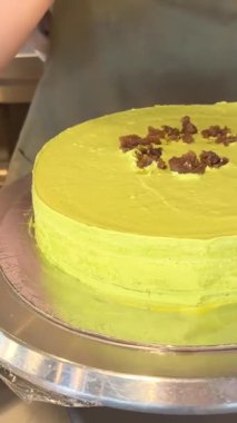 Odaklanmış ev hanımı, iki katlı pastayı sarımsı limonlar ve yeşil yapraklı pastalarla süslüyor. Mutfakta duran sarışın kadın doğum günü partisi için özel şekerleme hazırlıyor.