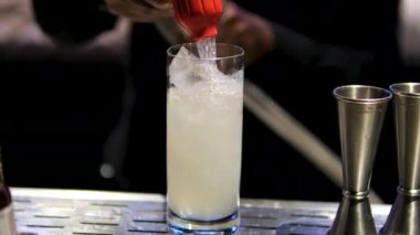Barmen buzları barda kokteyl yapıyor. Bardaki barmenin önünde buzla dolu alkollü içecekler için çeşitli bardaklar. Bir bardağa soda dök.