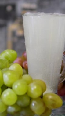 Taze harmanlanmış, tohum ve bardaktaki deri parçalarıyla dolu kalın üzüm suyu. Cam bir kasede üzüm demetleri ve masada üzümlü meyveler. Aspirin tableti bardakta köpürüyor.