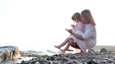 Beyaz elbiseli anne ve kız gün batımında okyanus kıyısında el ele tutuşarak kumda yalınayak koşuyorlar. Çocuk rüya konsepti. Mutlu aile küçük kız ve anne yalnız doğa ile rahatlayın gün batımı 