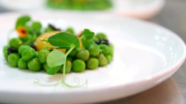 Yenilebilir çiçekler ve mikroyeşilliklerle dolu bir tabakta çiğ yumurta sarısı ile bezelye sunumu. Yeşil bezelye restoranı. Yüksek kalite 4k görüntü