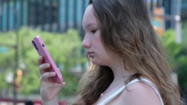 Genç İspanyol kadın cep telefonu kullanırken yürüyor. Şehirde gülümseyen mutlu üniversite öğrencisi kız. Yüksek kalite 4k görüntü