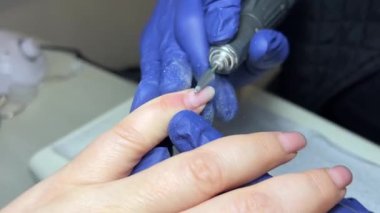 Manikürcü, profesyonel bir elektrikli tırnak törpüsü yardımıyla müşterilerin çivilerinin eski kaplamasını öğütüyor. Yüksek kalite 4k görüntü