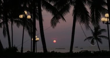 Endonezya sahilinde gün batımı. Akşam gökyüzündeki büyük güneş ufka dokunuyor. Hint Okyanusu 'ndaki Palm Beach' in arka planı. Kumda dalgalar üzerinde güneş izleri. Doğa inanılmaz turuncu gün batımı 