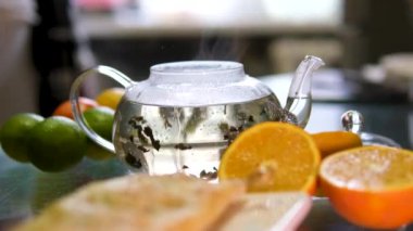 Mutfak masasında bitkisel çay standı olan cam çaydanlık. Çay demlenir ve aroması mutfağı doldurur. Lezzetli ve aromatik içeceklerden hoşlanır. Yüksek kalite 4k görüntü