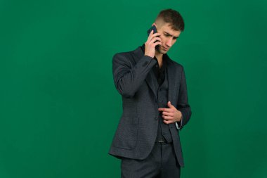 Yeşil arka plandaki yakışıklı bir adamın duyguları. Koyu renk, yakın plan, genç adam. Elden konuşma, SMS 'i ara, internetten arama cihazı, patronun iş ilanı.