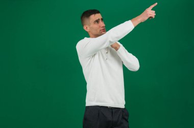 Boş yere parmak gösteren, düşük fiyatlı alışveriş tavsiyesi veren sıradan kot gömlek giyen, izole edilmiş yeşil arka planı olan harika bir adamın fotoğrafı. Yüksek kalite fotoğraf