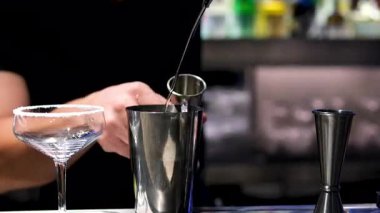 Barmen kokteyl yapımında kullanılan malzemeleri ölçmek için jigger kullanır ve yavaş çekimde sallanan sıvıları yakın çekime döker. Barmenler için profesyonel eğitim. Yüksek kalite 4k görüntü