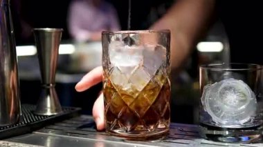 Profesyonel bir barmene yakın plan, alkol kokteyli ile profesyonel kristal uzun süreli buz küplerini bardaki veya disko kulübündeki müşterilerle karıştırıyor. Profesyonel barmen ustaca yaratıyor.