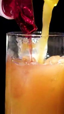 Bardaki barmen ferahlatıcı bir portakal kokteyli hazırlıyor, kırmızı bir kokteyl ile buz küplerini ustalıkla karıştırıyor. Kapatın. Ağır çekim. Yüksek kalite 4k görüntü