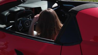 Genç, beyaz bir kadın, yol gezisinde kırmızı bir ciple güneşli bir sahil yolculuğunun tadını çıkarıyor. Neşeli ifadesi ve barış işareti kaygısız bir yolculuğun özünü yansıtıyor, ağır çekimde. Kırmızı kadın arabası.