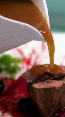 Mutfakta yemek pişiren mavi eldivenli profesyonel bir aşçı. Erkek eller lezzetli sosu kızarmış et ve kızarmış meyve ile dolduruyor, Yavaş çekim yemek videosu. hd. Yüksek kalite 4k görüntü