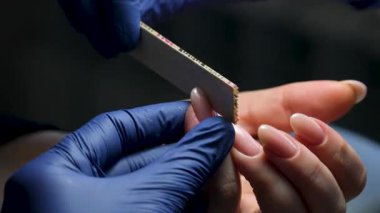 Güzellik salonundaki manikür ustasının manikür adım adım bütün hareketleri tırnak derisi lekesi temizleme jöle güçlendirici kadınların ellerini mavi eldivenlerle güçlendirme öz bakım sağlığına. Yüksek kalite 4k görüntü