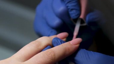 Güzellik salonundaki manikür ustasının manikür adım adım bütün hareketleri tırnak derisi lekesi temizleme jöle güçlendirici kadınların ellerini mavi eldivenlerle güçlendirme öz bakım sağlığına. Yüksek kalite 4k görüntü