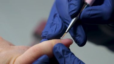 Güzellik salonundaki manikür ustasının manikür adım adım bütün hareketleri tırnak derisi lekesi temizleme jöle güçlendirici kadınların ellerini mavi eldivenlerle güçlendirme öz bakım sağlığına. Yüksek kalite 4k görüntü