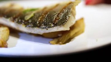 Süslü bir restoranın masasındaki beyaz tabağa yakın bir yerde. Izgara beyaz balık tabağı.