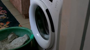 Kız çamaşırları çamaşır makinesinde yıkıyor ve çamaşırları çamaşır ipine asıyor. Bahçede güneşli bir gün. Çamaşır askısında renkli kumaş havlular, yeşil çimenler..