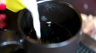 Latte sanatı yapılıyor. Cafe 'de yapılan kahve sanatının yakın çekim videosu. Süt, beyaz bardağa kahve ile dolduruluyor ve güzel bir latte sanatı yaratıyor. Bir fincan sade kahveye süt dök.