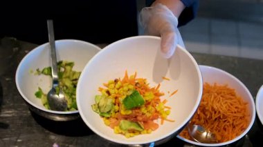 Sebzeli bir kase salata yapmak yeşillik, mayonez sosu, salatalık havucu, avokado ve mısır unu eldivenle hazırlamak, salata aşçısını elleriyle süslemek. Yüksek kalite