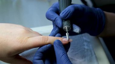 Mavi eldivenli bir manikür ustasının ellerini yakın plan bir güzellik salonundaki tırnak altlarını budamak ve sökmek için elektrikli tırnak törpüsü kullanıyor. Donanım manikürü. Yüksek kalite 4k görüntü