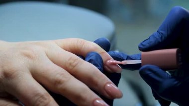 Tırnak cilası başvurusu: Bir manikürcünün müşteri tırnağına ince bir katman çıplak tırnak cilası sürmesi. Titiz fırça darbeleri, tırnak sanatının hassas sürecini vurgular..