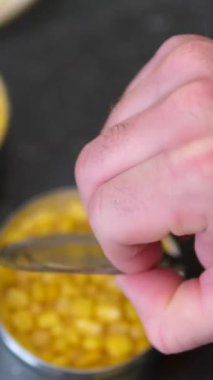 Top View Man 'in elleri mısır kavanozunu açıyor. Koyu arkaplanda izole edilmiş metal kavanozdaki konserve mısır. Konserve açacağıyla bir konserve kutusu aç.