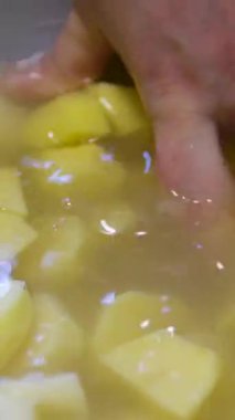 Dişi eller soğuk suda dilimlenmiş patatesi buzla yıkıyor, yemek hazırlıyor. Ağır çekimde yakın çekim. Yüksek kalite 4k görüntü