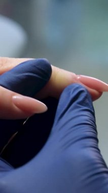 Güzellik salonundaki manikür ustasının manikür adım adım bütün hareketleri tırnak derisi lekesi temizleme jöle güçlendirici kadınların ellerini mavi eldivenlerle güçlendirme öz bakım sağlığına. Yüksek kalite 4k görüntü