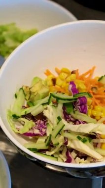 Sebzeli bir kase salata yapmak yeşillik, mayonez sosu, salatalık havucu, avokado ve mısır unu eldivenle hazırlamak, salata aşçısını elleriyle süslemek. Yüksek kalite