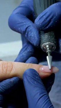 Mavi eldivenli bir manikür ustasının ellerini yakın plan bir güzellik salonundaki tırnak altlarını budamak ve sökmek için elektrikli tırnak törpüsü kullanıyor. Donanım manikürü. Yüksek kalite 4k görüntü