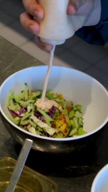 Sebzeli bir kase salata yapmak yeşillik, mayonez sosu, salatalık havucu, avokado ve mısır unu eldivenle hazırlamak, salata aşçısını elleriyle süslemek. Yüksek kalite