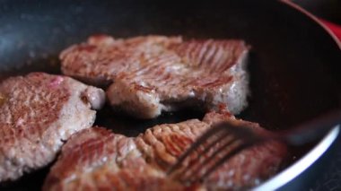 Bir şef mutfaktaki bir tavada biftek pişirir ve onu diğer tarafa çevirir, yakın plan yemek. Lezzetli biftek yapma süreci. Yüksek kalite 4k görüntü