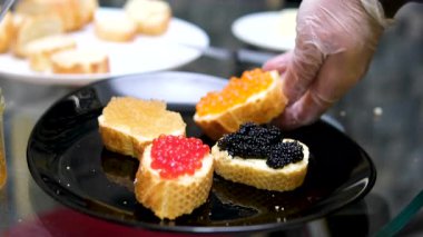 Ahşap bir masada tereyağlı kırmızı havyarlı sandviç hazırlayan ellerin yakın çekimi. Kremalı tereyağı ve parlak kırmızı balık yumurtası ile kaplı taze ekmek dilimleri. farklı havyar türleri 