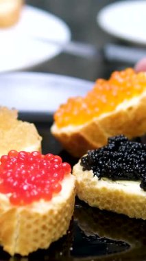 Ahşap bir masada tereyağlı kırmızı havyarlı sandviç hazırlayan ellerin yakın çekimi. Kremalı tereyağı ve parlak kırmızı balık yumurtası ile kaplı taze ekmek dilimleri. farklı havyar türleri 