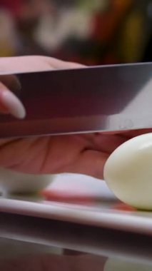 Dilimlenmiş yumurtaları tahta kesme tahtasına yerleştiren eller. Yemek hazırlıkları sırasında yumurta parçaları düzenleyen kişi. Mutfak işi için parmaklar yumurtaları dikkatlice tutuyor. Yemekleri düzenleyen eller