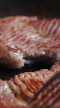 Bir şef mutfaktaki bir tavada biftek pişirir ve onu diğer tarafa çevirir, yakın plan yemek. Lezzetli biftek yapma süreci. Yüksek kalite 4k görüntü
