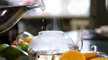 Portakallı, limonlu ve limonlu çayı şeffaf çaydanlıktan bardağa doldurmak. Arka planda bal ve krep ile çay demlemek. Yavaş çekim çayı. Tam HD. Yüksek kalite 4k görüntü