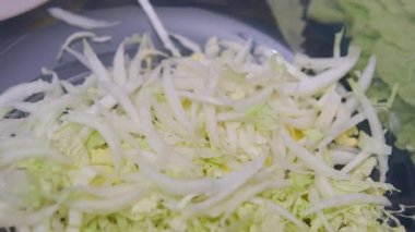 Ev hanımı sebze salatası yapmak için beyaz lahanayı ince ince keser. Mutfak masasındaki tahta kesme tahtasının üzerinde beyaz lahana doğrayan kadın ellerinin yakın çekimi. Vejetaryenlik kavramı 