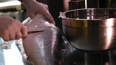 Sabit bir alçak çekim, taze somon balığını kesmeye başlayan bir şefi yakalar, balık hazırlıktaki hassasiyet ve tekniği vurgular. Mutfak, deniz ürünleri ve profesyonel mutfak içeriği için ideal..