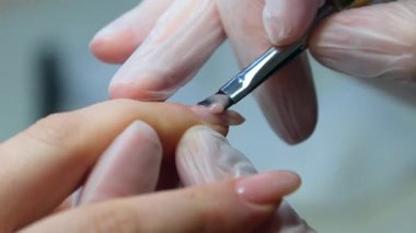 Manikürcü müşterilerin tırnaklarını renksiz cila ile boyuyor. Tırnak sanatları ustası kızların eline şeffaf bir manikür yapıyor. Bir kadın kuaförde tırnaklarına bakar..