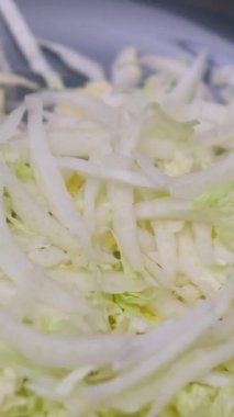 Ev hanımı sebze salatası yapmak için beyaz lahanayı ince ince keser. Mutfak masasındaki tahta kesme tahtasının üzerinde beyaz lahana doğrayan kadın ellerinin yakın çekimi. Vejetaryenlik kavramı 