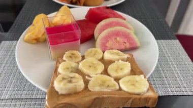 Muz ve bal dilimli tam tahıllı tost. Koyu tabakta granola ile servis ediliyor. Dengeli beslenme için besleyici kahvaltı seçenekleri. Yüksek kalite 4k görüntü