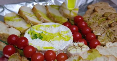  Konum. Bir ev hanımı mutfak masasındaki salataya zeytinyağı ekler. Genç bir kadın çeşitli sebze ve peynirlerle zeytinyağı döküyor. Domatesli ve kızarmış ekmekli camembert peyniri pişir.