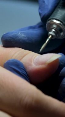 Kadın eli ve manikür aletleri, güzellik salonunda manikür yapma süreci. Güzellik salonunda çivi bakım prosedürü. Eldiven giymiş deneyimli bir manikürcünün eldivenli elleri cilalanmış naie 'dir.