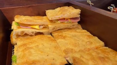 Focaccia sandviç yığını, mortadella ile doldurulmuş, birbiri üzerine istiflenmiş, arka planda Noel ağacı olan bir tahta kesme tahtasının üzerinde fotoğraflanmış.