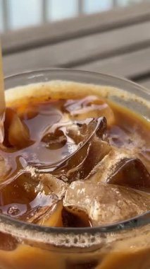 Kadın eli, tropik deniz manzaralı kafedeki ahşap masaya kokteyl ve metal pipetle birlikte uzun camlar koyuyor. Okyanuslu çatı restoranındaki bardak altlığına buzlu kahve ya da smoothie koymak. 