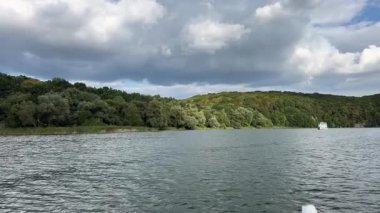 Ufuk çizgisine doğru İHA uçuşu ve Illinois Ormanı 4k 'ta açık yeşil yapraklı, beyaz kabarık bulutlu ve mavi gökyüzlü bir göl üzerindeki ağaç hattı. Yüksek kalite 4k görüntü